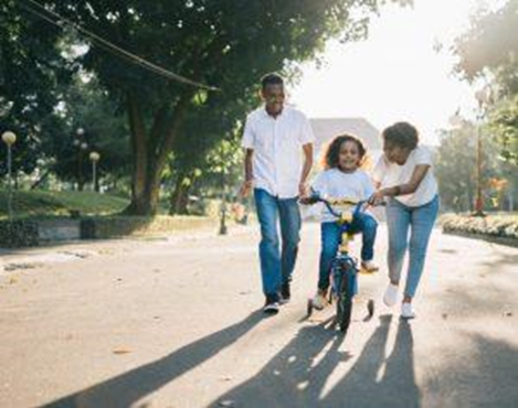 Man standing beside his wife teaching their daughter how to ride a bicycle.